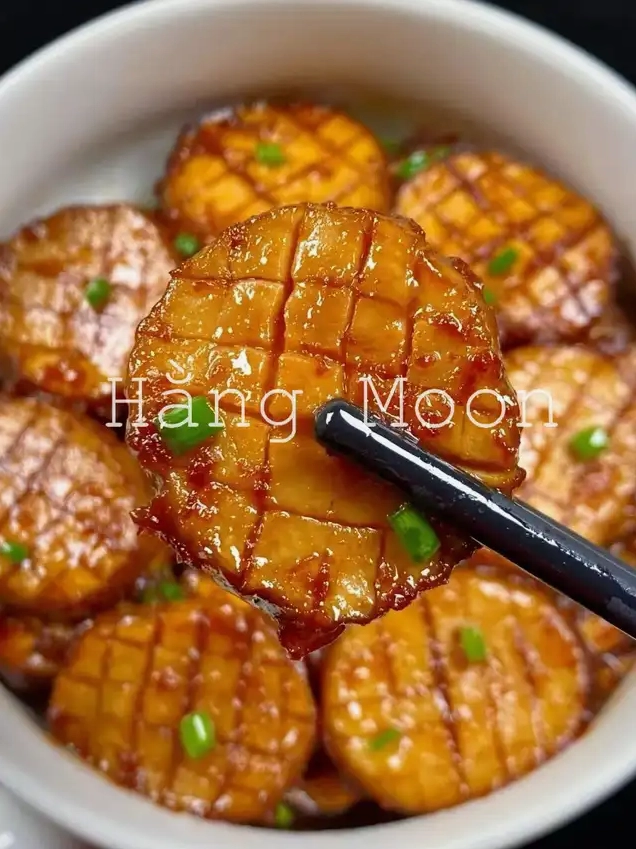 Cận cảnh một lát nấm đùi gà sốt nước tương bóng bẩy được gắp bằng đũa đen Lát nấm có những đường khứa đẹp mắt và được trang trí bằng hành lá