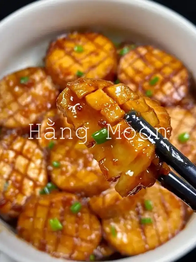 Cận cảnh một miếng nấm đùi gà sốt nước tương được gắp bằng đũa cho thấy rõ kết cấu bên trong của nấm và lớp sốt đậm đà óng ánh bên ngoài