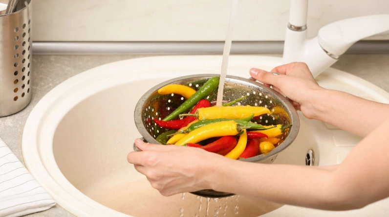 Hình ảnh đôi tay đang rửa sạch ớt nhẹ nhàng dưới vòi nước để loại bỏ bụi bẩn
