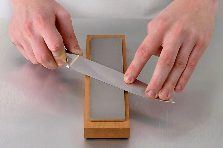 Một người đang tập trung cao độ mài chiếc dao thái thịt thật sắc bén